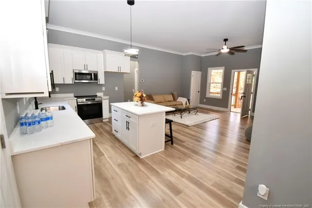 a open kitchen with a sink dishwasher a stove and white cabinets with wooden floor