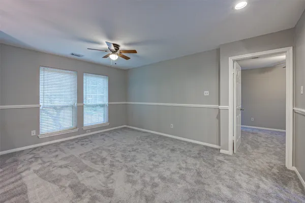an empty room with chandelier fan and windows