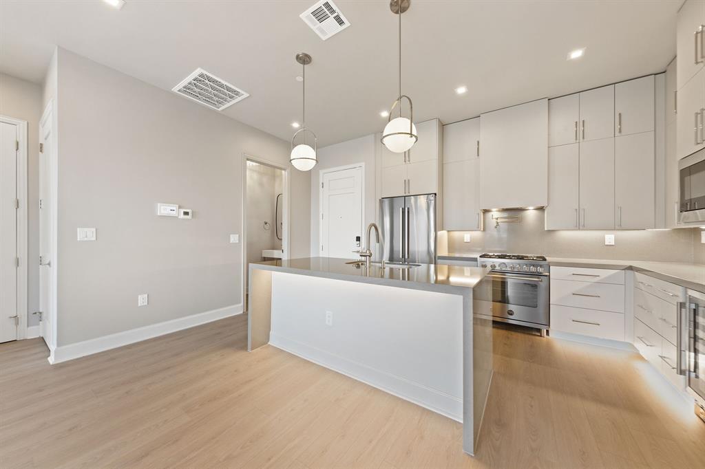 1900 South Ervay Street, Unit 508 Dallas, TX 75215 - Photo 3 of 36 a large white kitchen with kitchen island a stove a sink a refrigerator and white cabinets with wooden floor