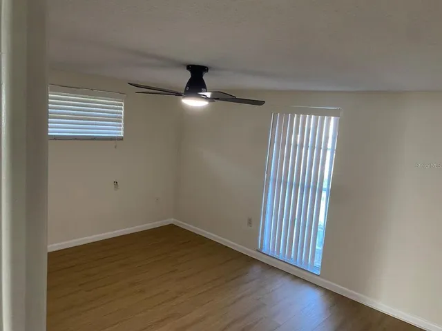 an empty room with wooden floor fan and windows