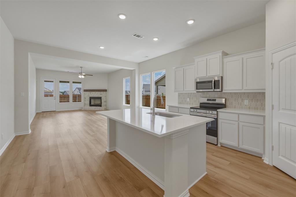 1217 Colca Drive Springtown, TX 76082 - Photo 7 of 25 Open-concept living space featuring wood-finish flooring, a kitchen island with a sink, white cabinetry, stainless steel appliances, and a fireplace with a stone surround