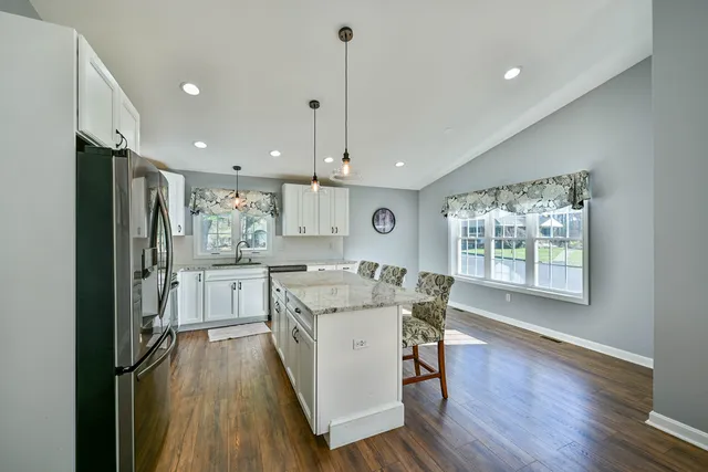 a kitchen with stainless steel appliances granite countertop a refrigerator a sink dishwasher a stove and a dining table with wooden floor