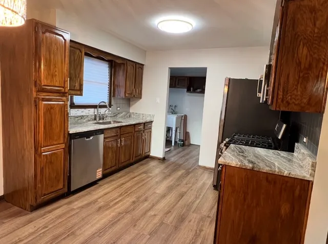 a kitchen with stainless steel appliances granite countertop wooden cabinets a refrigerator a sink a stove a microwave and wooden floors