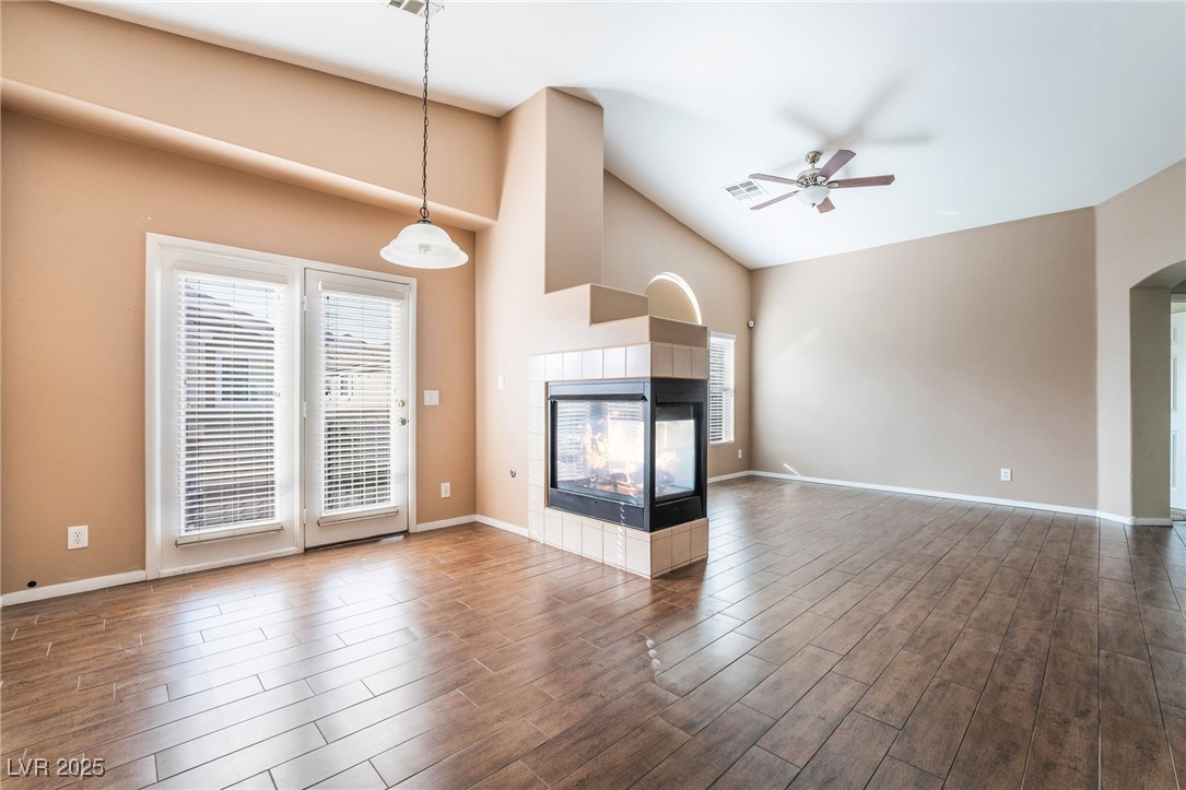 1570 Rusty Ridge Lane Henderson, NV 89002 - Photo 3 of 35 Unfurnished living room with dark wood-type flooring, a tile fireplace, a ceiling fan, and a healthy amount of sunlight