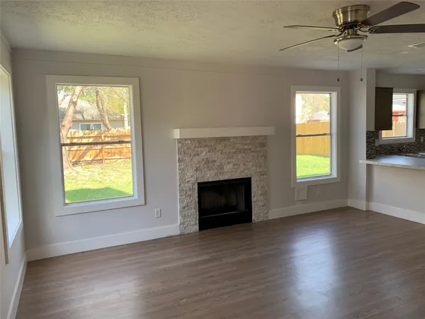 a view of an empty room with wooden floor fireplace and a window