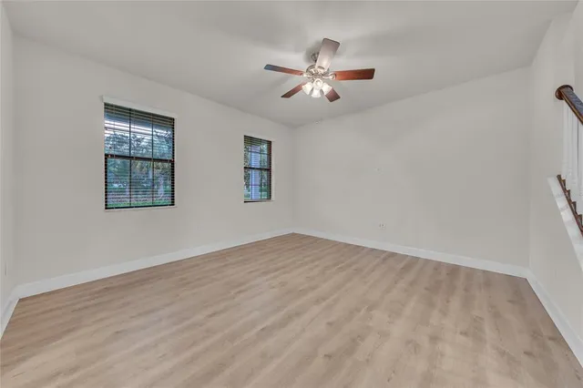 a view of an empty room with chandelier fan and wooden floor
