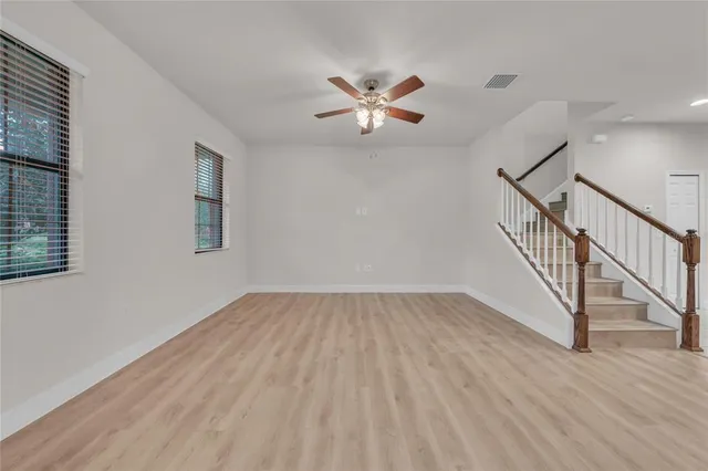 a view of an empty room with wooden floor and a ceiling fan