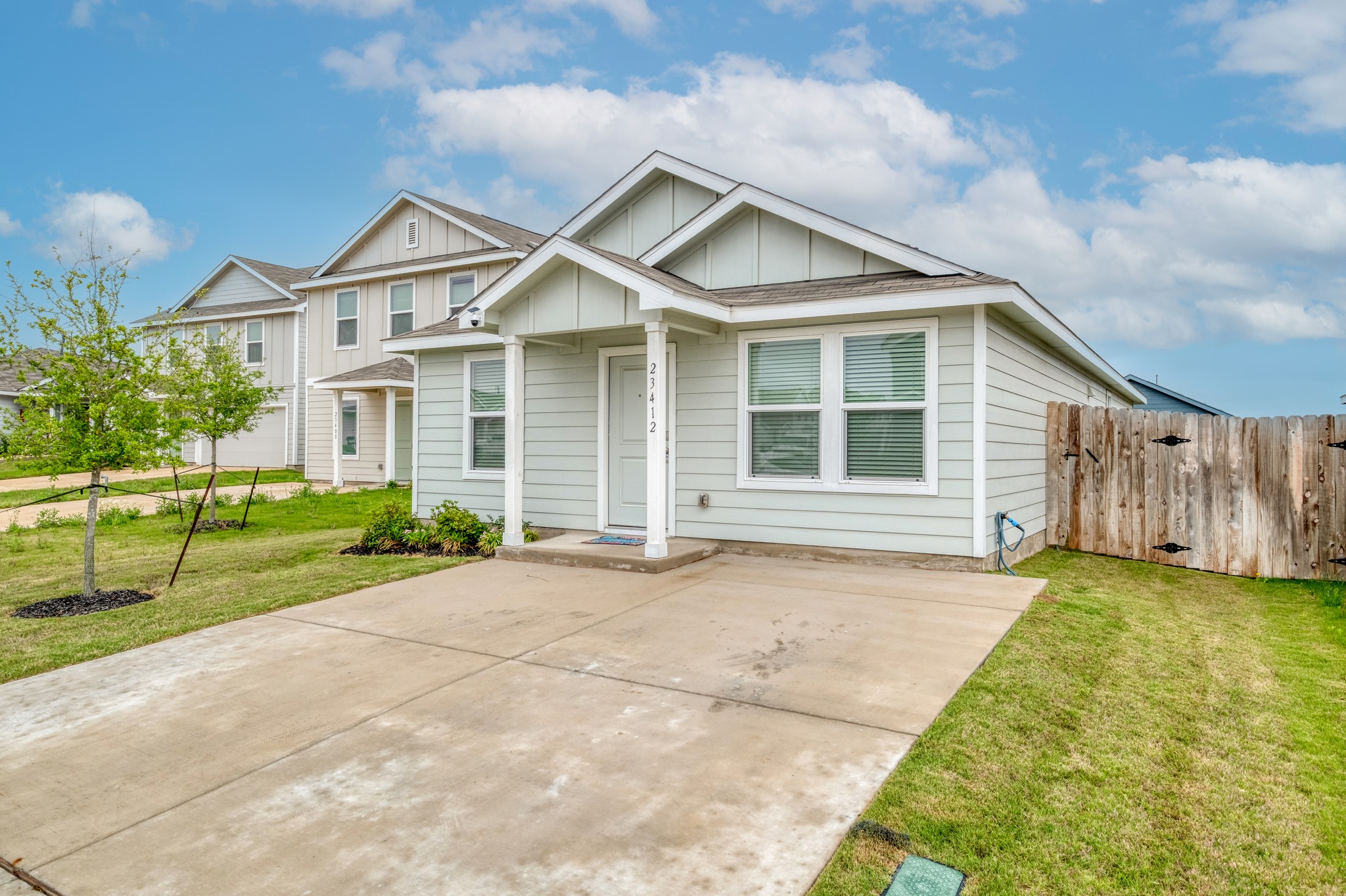 23412 Tiny Moons Way Elgin, TX 78621 - Photo 4 of 38 Light-colored siding exterior with a covered front porch, a concrete driveway, a wood fence, and a manicured lawn