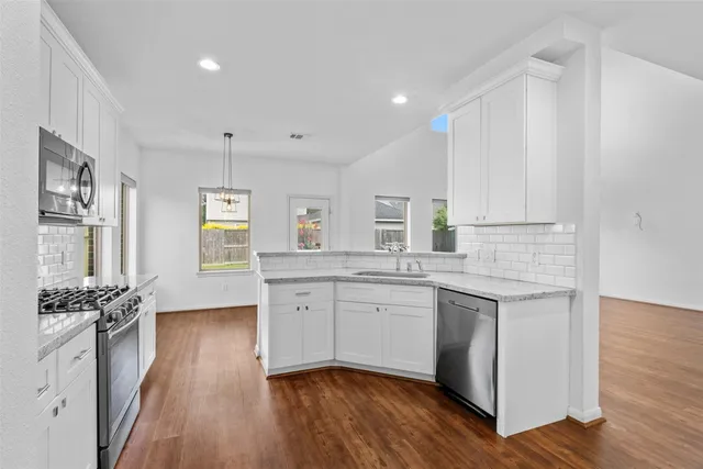 a kitchen with a sink dishwasher wooden floor and white cabinets