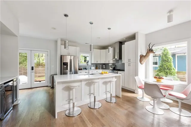 a kitchen with stainless steel appliances kitchen island granite countertop a refrigerator a stove a dining table and chairs with wooden floor