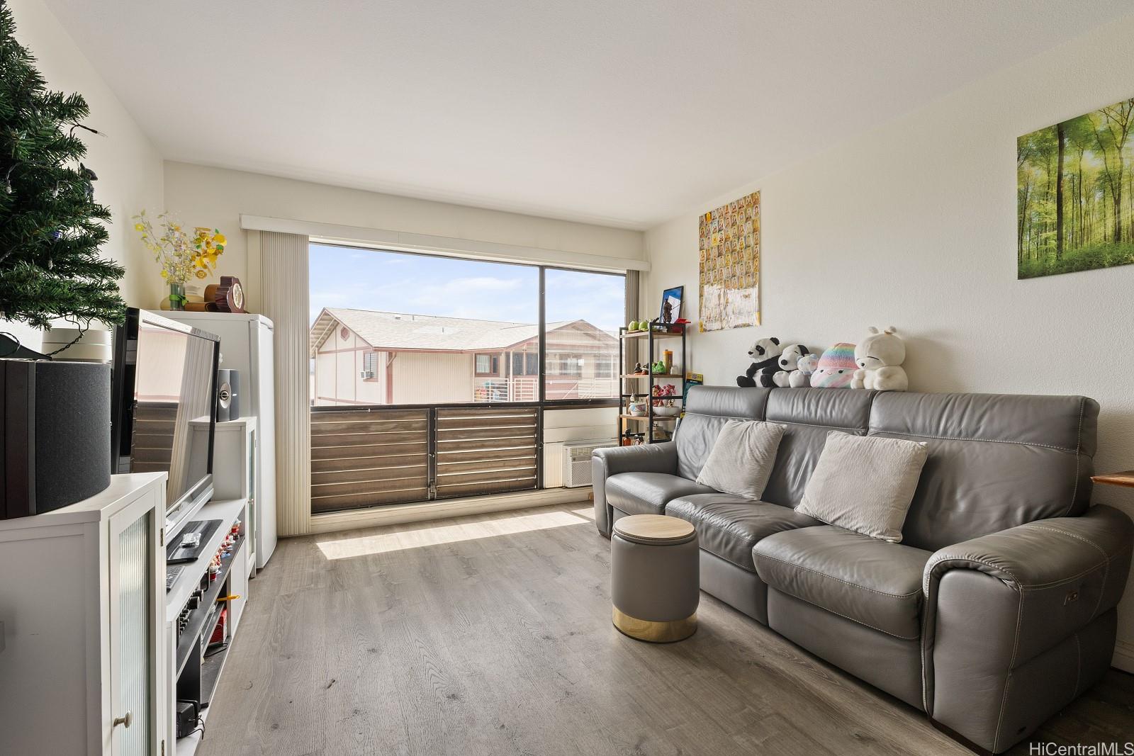 98-660 Moanalua Loop, Unit 276 Aiea, HI 96701 - Photo 2 of 25 a living room with furniture a flat screen tv and a floor to ceiling window