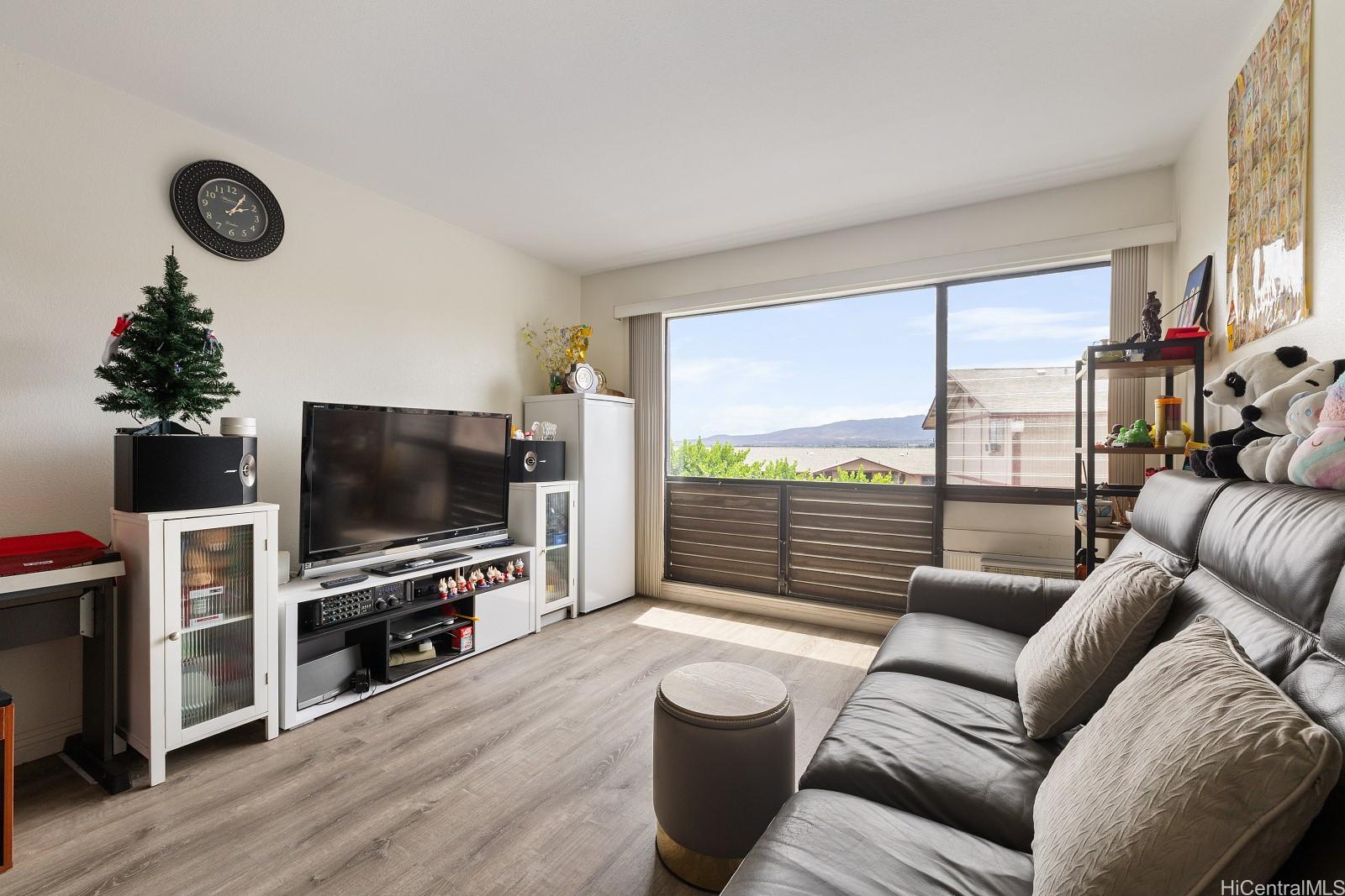 98-660 Moanalua Loop, Unit 276 Aiea, HI 96701 - Photo 3 of 25 a living room with furniture a flat screen tv and a floor to ceiling window