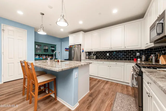 a kitchen with stainless steel appliances kitchen island granite countertop a stove a sink a refrigerator and white cabinets with wooden floor