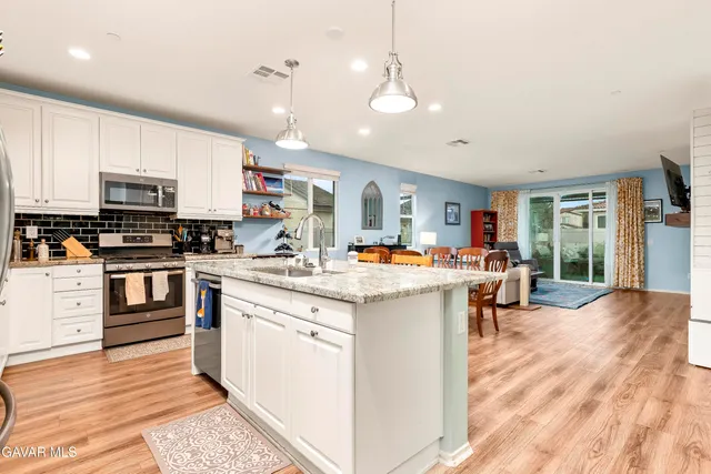 a kitchen with stainless steel appliances kitchen island granite countertop a stove top oven a sink a dining table and chairs with wooden floor