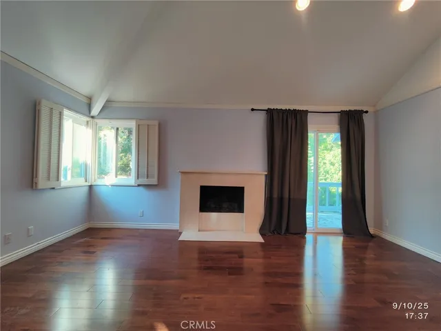 an empty room with wooden floor fireplace and windows