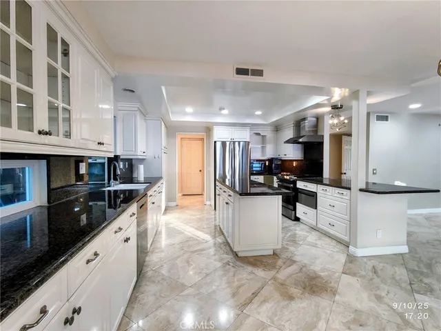 a kitchen with stainless steel appliances kitchen island granite countertop a refrigerator a stove top oven a sink a dining table and chairs with wooden floor