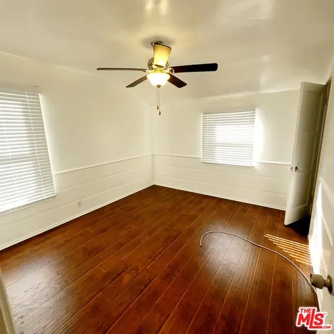 an empty room with wooden floor fan and windows