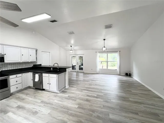 a large kitchen with stainless steel appliances granite countertop a stove a sink white cabinets and wooden floor