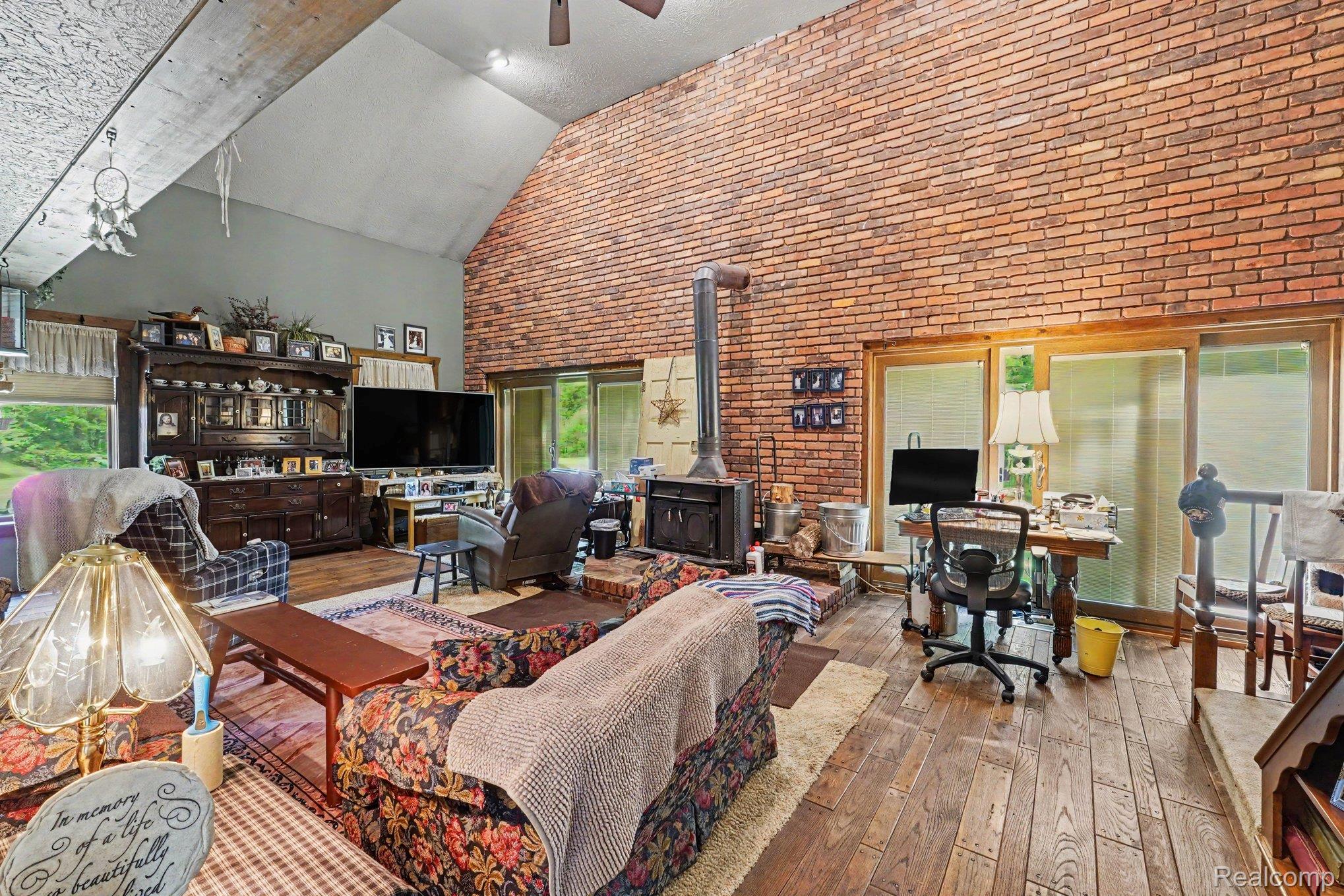 3284 Pratt Road Metamora, MI 48455 - Photo 4 of 17 Vaulted ceiling with exposed wood beams, brick accent wall, wood-finish flooring, and a freestanding wood-burning stove