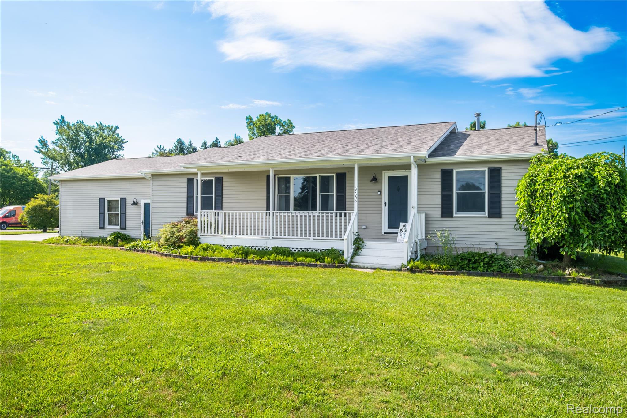 9600 Hamill Road Otisville, MI 48463 - Photo 25 of 32 Single-story residence featuring light-colored siding, a covered front porch with white railings, a gray shingle roof, black window shutters, and a green lawn