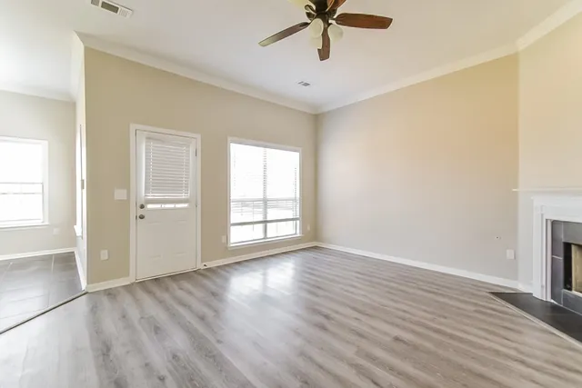 an empty room with wooden floor fan and windows