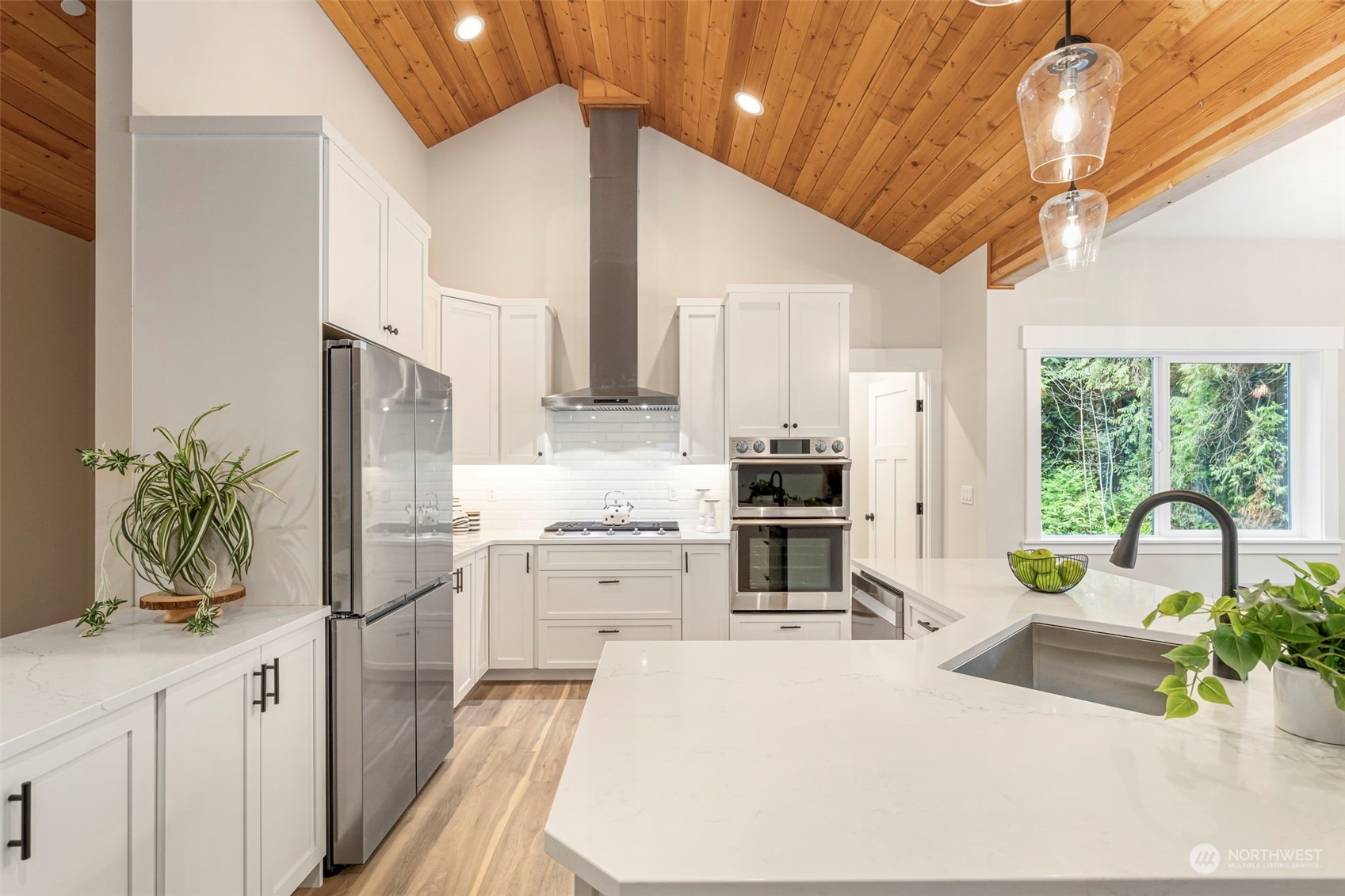 22086 Dewberry Road Northeast Indianola, WA 98342 - Photo 13 of 40 a kitchen with stainless steel appliances kitchen island granite countertop a refrigerator a stove a sink dishwasher and white cabinets with wooden floor