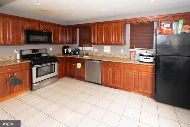 a kitchen with stainless steel appliances granite countertop a stove top oven a sink dishwasher and a refrigerator with wooden cabinets