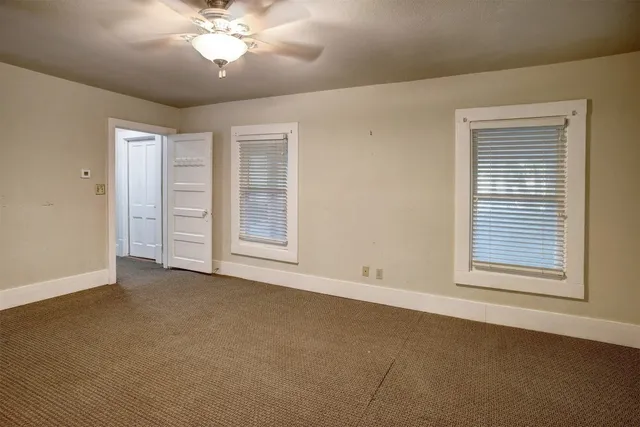 an empty room with chandelier fan and windows