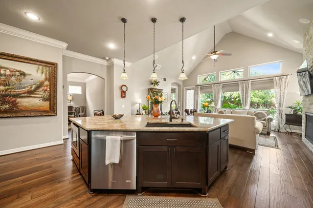 a kitchen with stainless steel appliances granite countertop a stove a sink dishwasher and a dining table with wooden floor