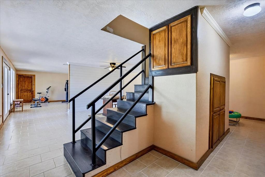 11591 Farm To Market 59 Athens, TX 75751 - Photo 22 of 40 WOW - fully air conditioned basement adds another 1565SF. Open-concept interior featuring a prominent staircase with black metal railings, wood finish treads, and integrated under-stair cabinetry. Large open spaces on each side of staircase, a full bathoom, utility room, and 2 more bedrooms. French doors lead outside.