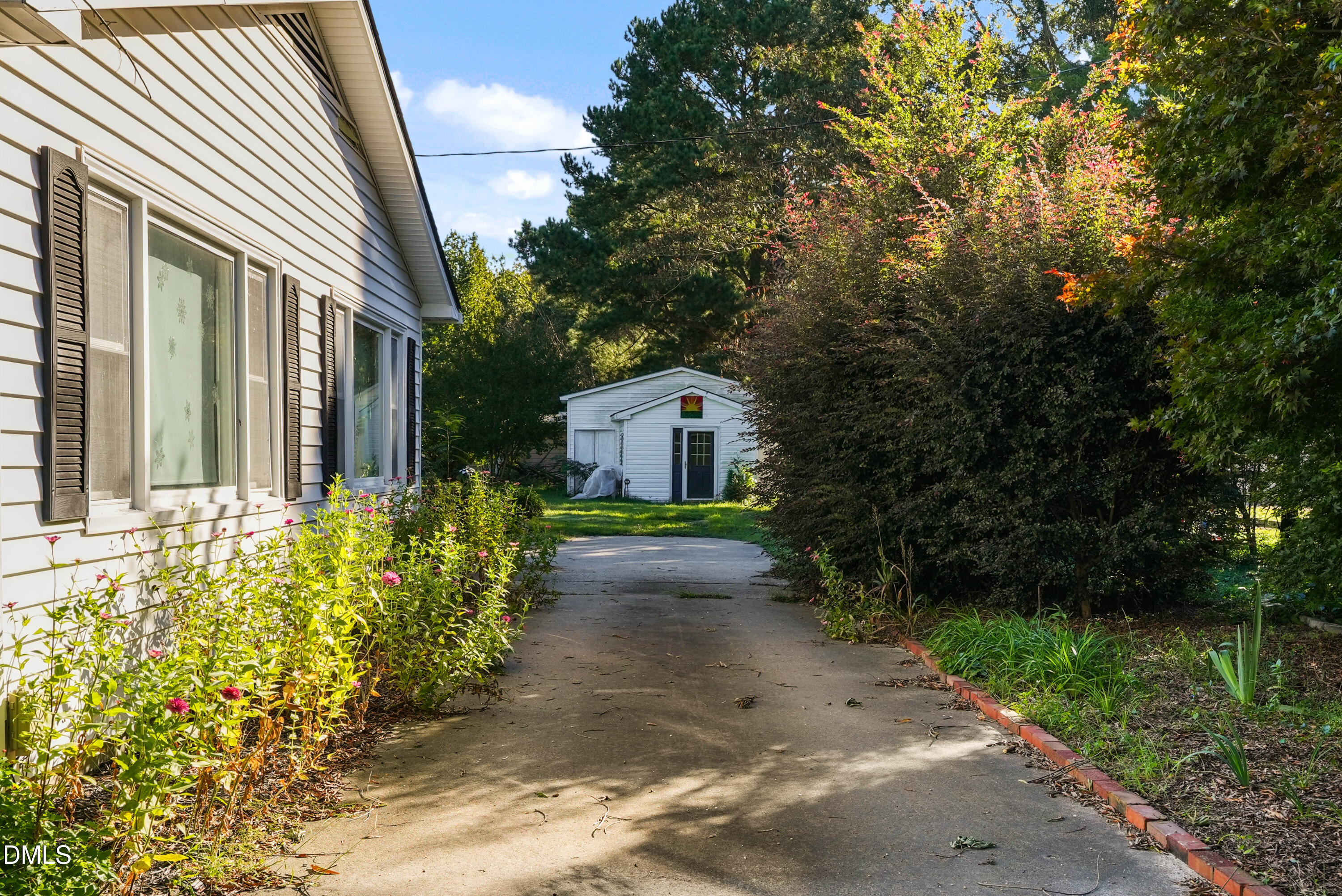 7406 Old Beulah Road Kenly, NC 27542 - Photo 5 of 30 White siding with dark shutters, paved walkway, mature landscaping, and a detached outbuilding