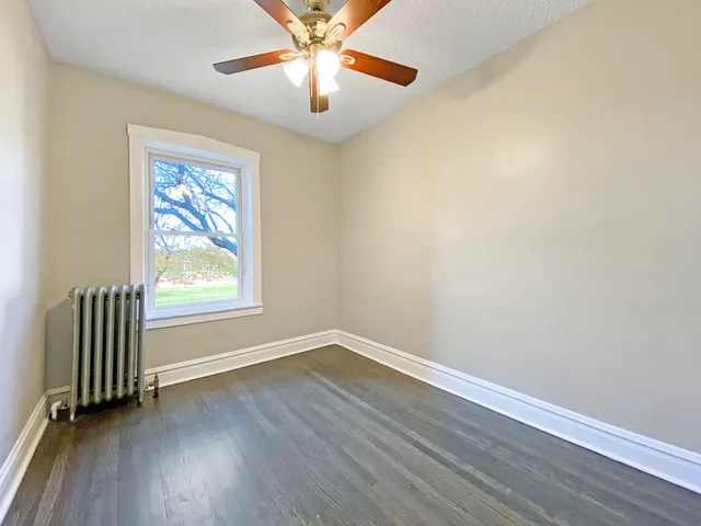 an empty room with wooden floor fan and windows