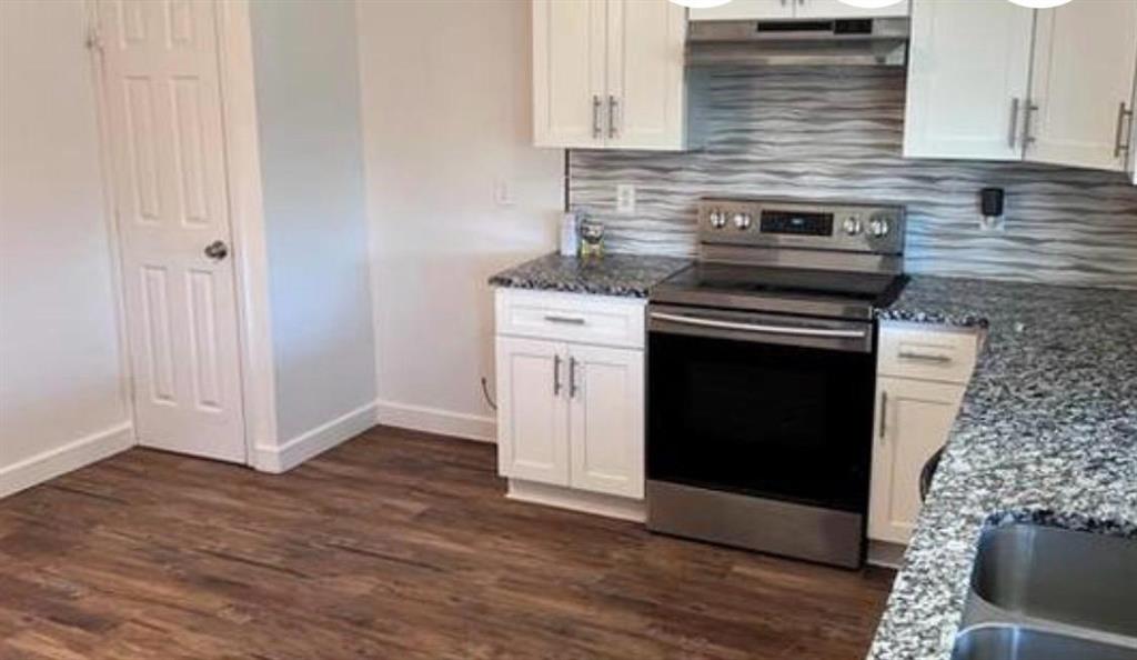 4422 Galaxie Road Garland, TX 75044 - Photo 7 of 11 Kitchen featuring wood-finish flooring, white cabinetry with silver hardware, granite countertops, a stainless steel range, and a textured backsplash