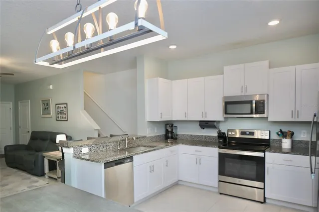 a kitchen with granite countertop a refrigerator a sink a stove a microwave a counter top space and cabinets