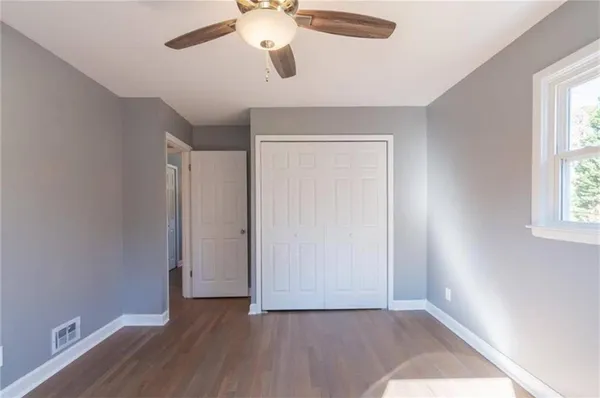 an empty room with wooden floor chandelier fan and windows
