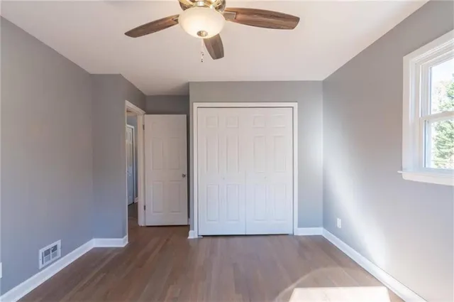 an empty room with wooden floor chandelier fan and windows