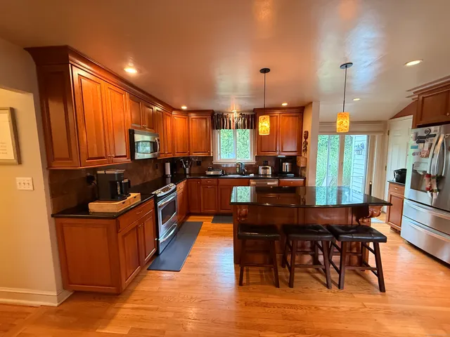 a kitchen with stainless steel appliances granite countertop wooden cabinets a refrigerator a stove a sink and dishwasher a oven with large windows