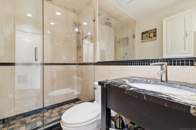 a bathroom with a granite countertop sink a toilet a mirror and shower