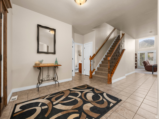255 East 1200 North Mapleton, UT 84664 - Photo 10 of 37 Inviting entry foyer featuring tile flooring, a carpeted staircase with wood handrails and wrought iron balusters, and a mountain backdrop visible through the large windows
