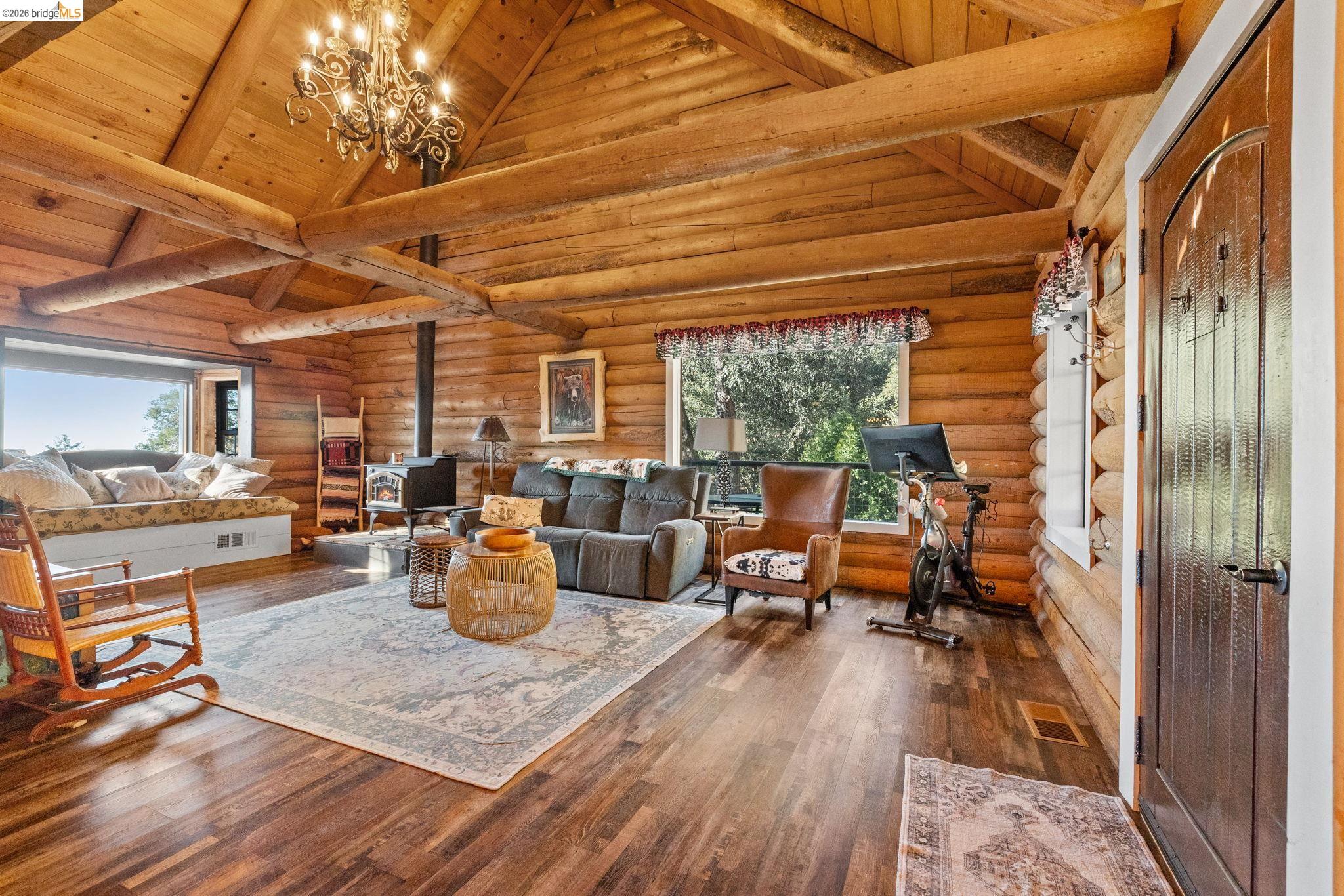 16144 Big Hill Road Sonora, CA 95370 - Photo 7 of 51 Vaulted wood-beam ceiling with chandelier, wood-finish flooring, built-in window seating, exposed log walls, and a freestanding wood stove