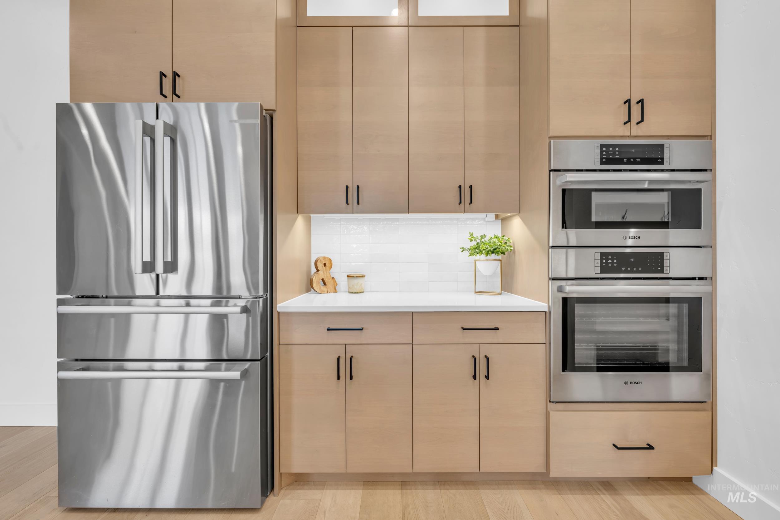 4447 East Copper Point Drive Meridian, ID 83642 - Photo 13 of 42 Kitchen with appliances with stainless steel finishes, backsplash, light brown cabinetry, light wood finished floors, and light stone countertops