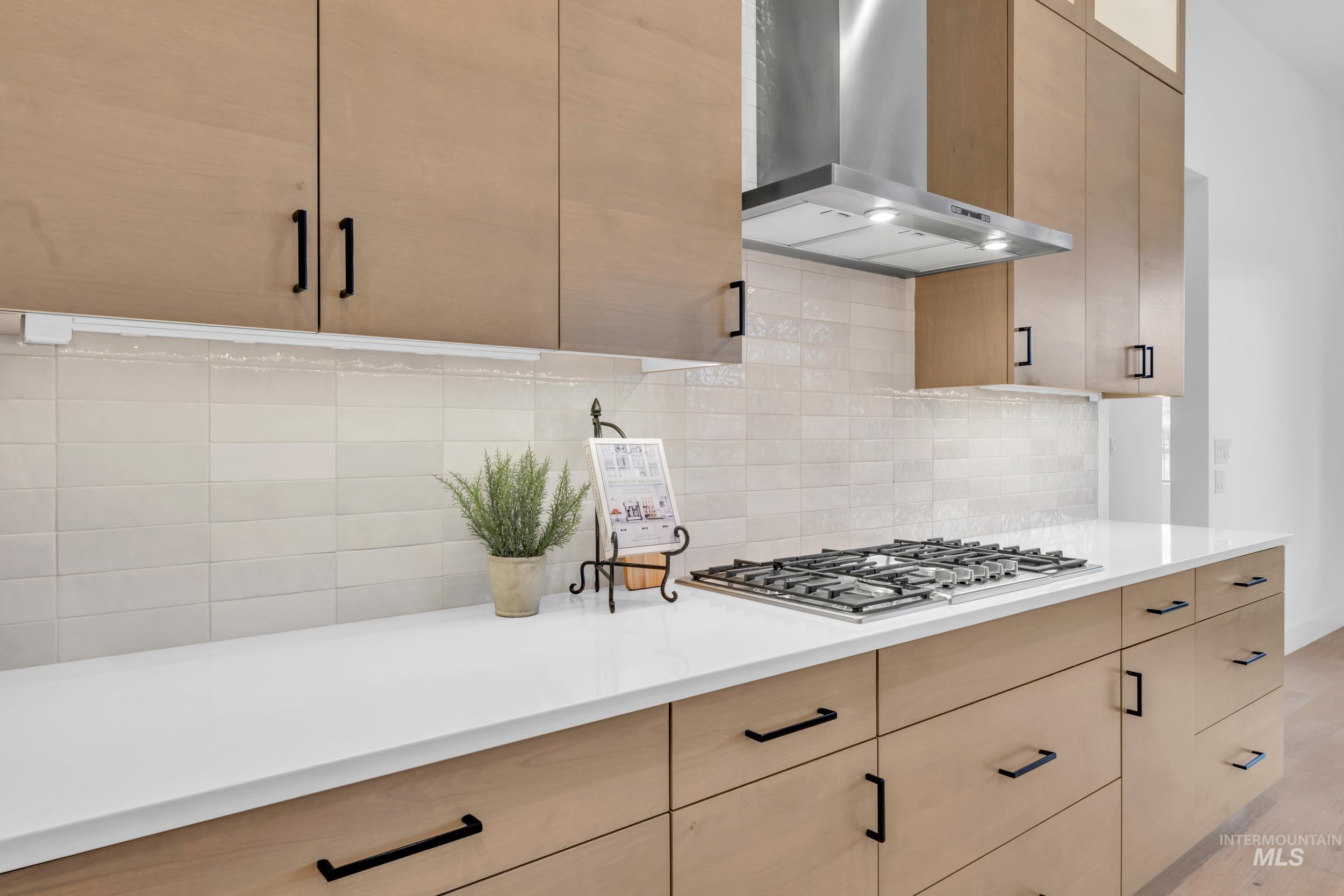 4447 East Copper Point Drive Meridian, ID 83642 - Photo 15 of 42 Kitchen featuring wall chimney exhaust hood, light brown cabinetry, backsplash, stainless steel gas cooktop, and modern cabinets