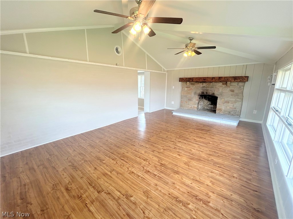 558 Lessig Avenue Akron, OH 44312 - Photo 11 of 15 Unfurnished living room featuring light wood-type flooring, a stone fireplace, vaulted ceiling, and a ceiling fan