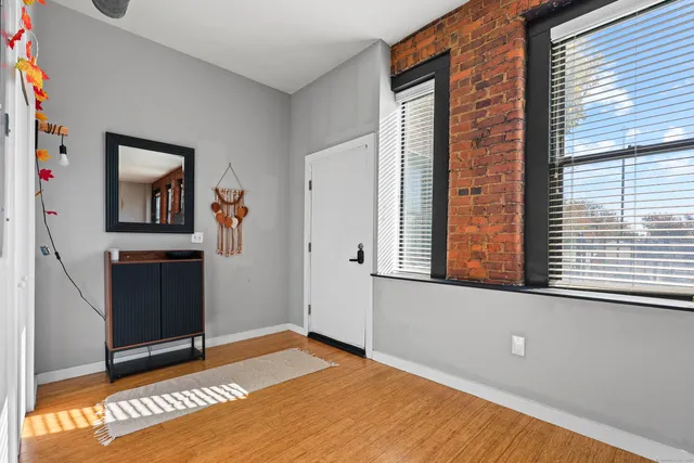 a view of an empty room with window and hardwood floor