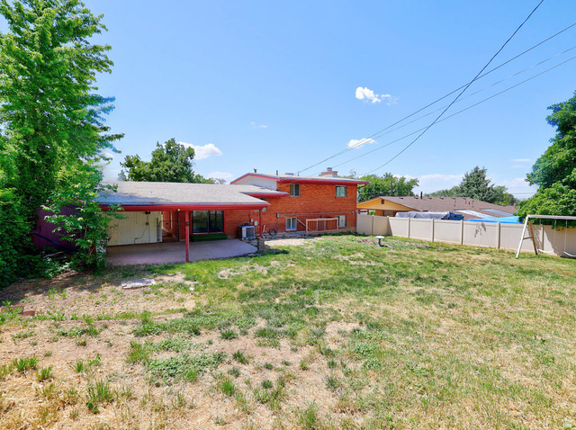 1272 Cook Street Ogden, UT 84404 - Photo 52 of 58 Expansive backyard featuring a covered patio with red support beams, a concrete slab, and an adjacent red brick exterior
