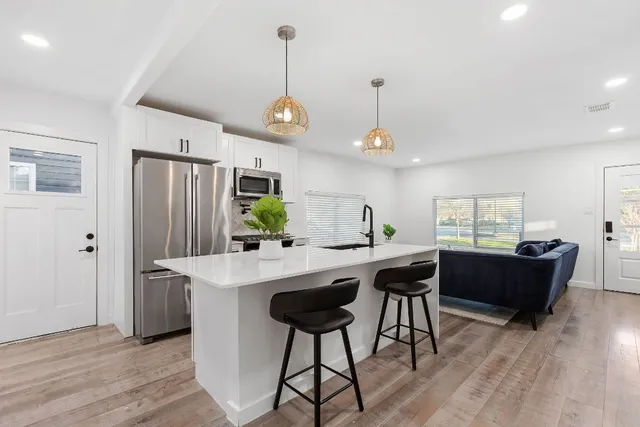 a kitchen with stainless steel appliances granite countertop a refrigerator a sink dishwasher a dining table and chairs with wooden floor