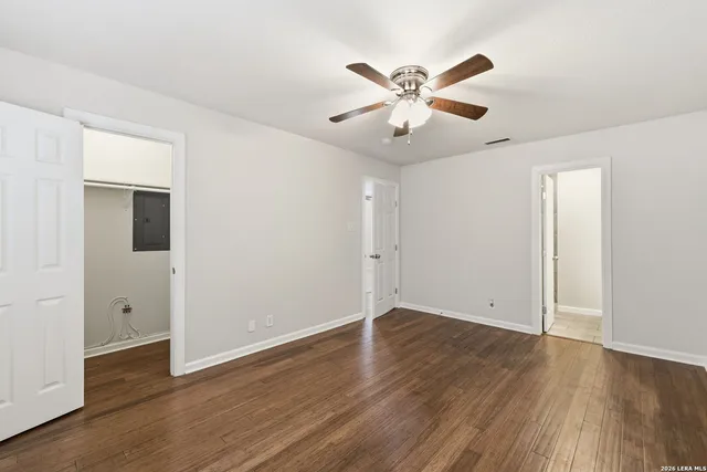 a view of an empty room with wooden floor and a ceiling fan