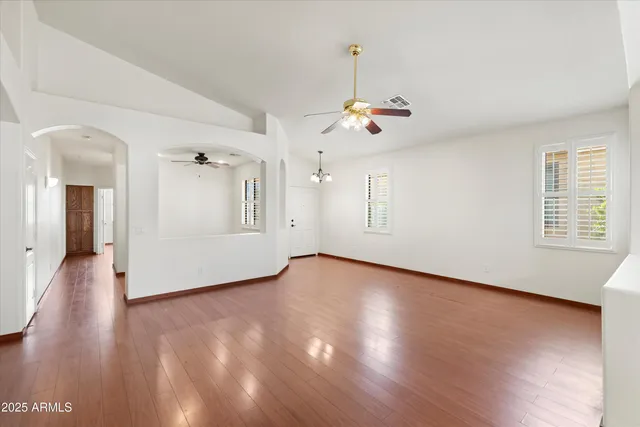 a view of an empty room with wooden floor and a ceiling fan