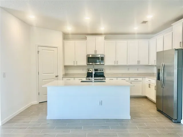 a kitchen with stainless steel appliances granite countertop a stove top oven a refrigerator a sink and dishwasher with white cabinets