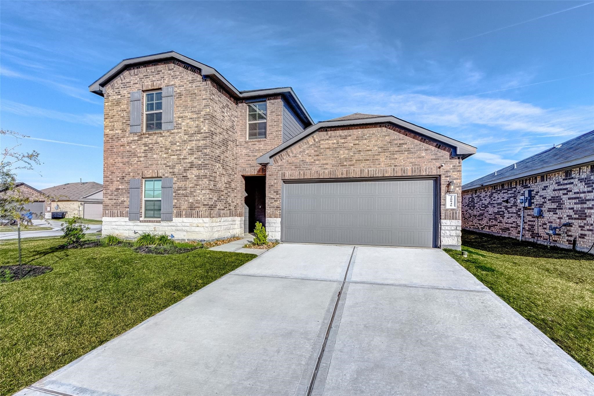 A modern two-story brick home with stone accents, a two-car garage, and a clean concrete driveway
